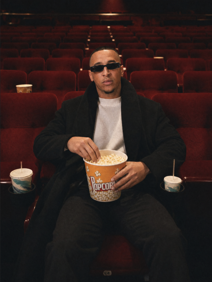 Portrait of director Riley Robbins seated in an empty cinema holding popcorn